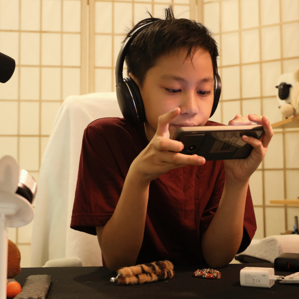 Student wearing headphones playing a mobile game—turn screen time into English learning.